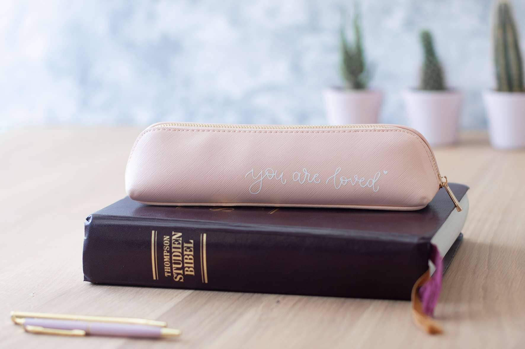 Schöner pinker Brillenetui mit "you are loved" Aufschrift auf einem Buch liegen.
