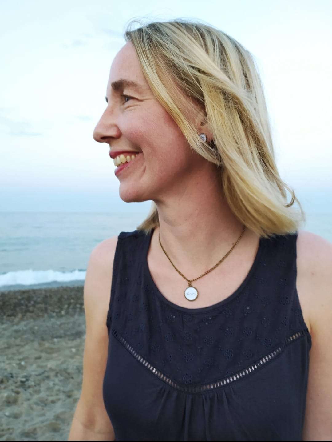Fröhliche Frau mit christlichem Schmuck am Strand, Glaube und Inspiration.