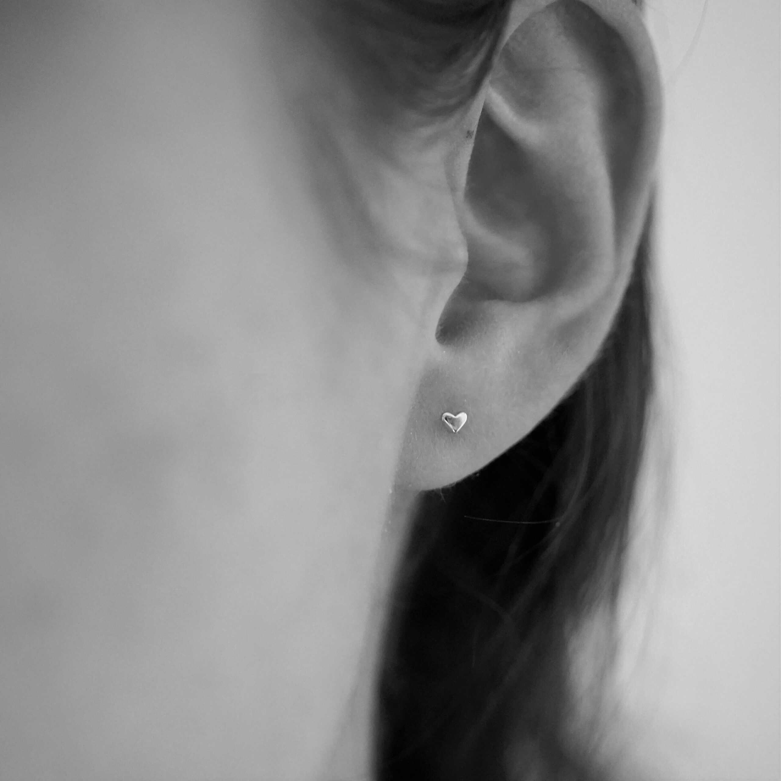 Schimmerndes Herz-Ohrring an weiblichem Ohr, christlicher Schmuck, Damenaccessoire.