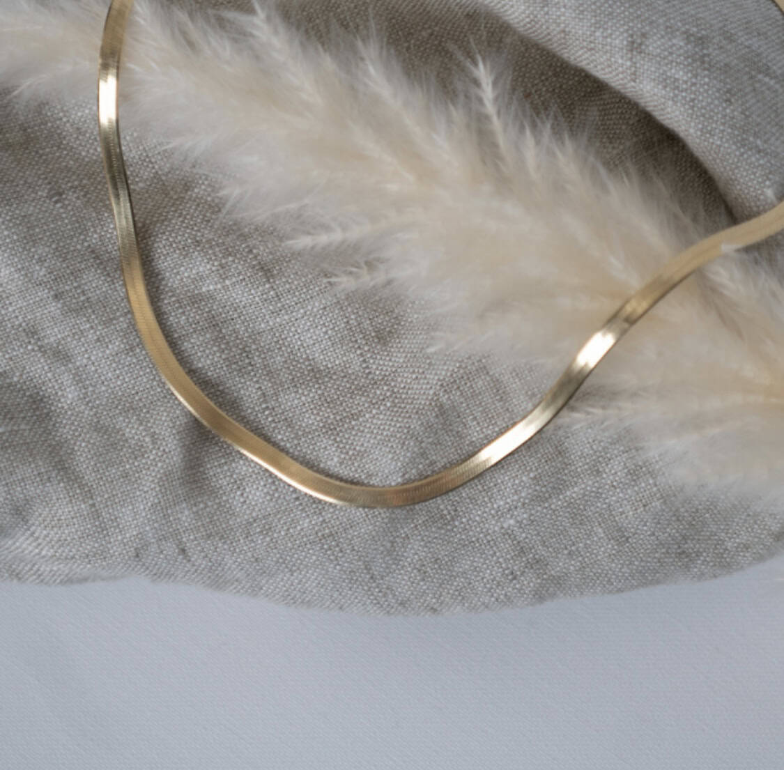 Feathered gold necklace on neutral fabric, christliche Schmuckmarke, spiritueller Stil.