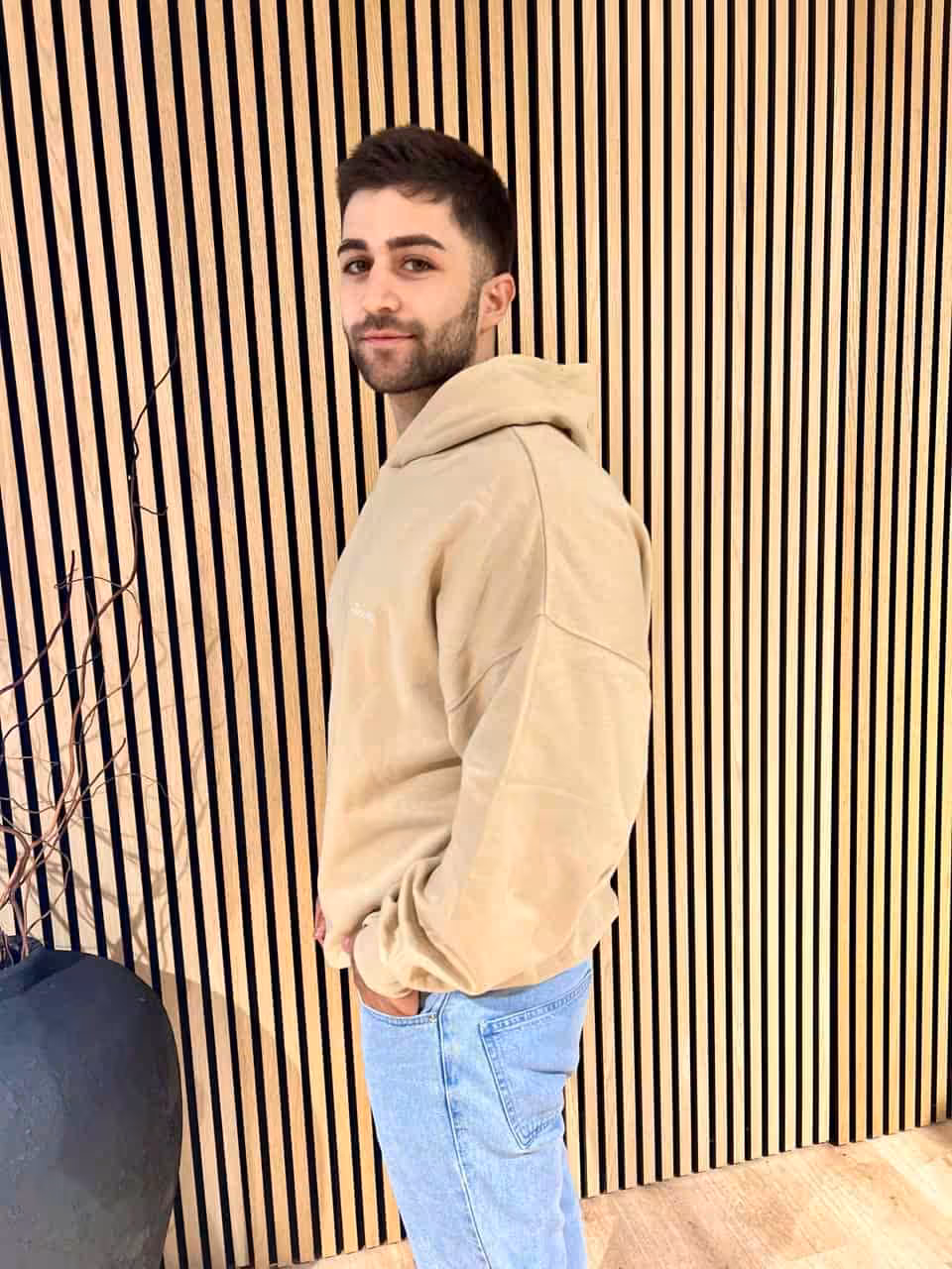 Modisch gekleideter junger Mann vor Holzverkleidung, casual Streetwear, moderne Mode, urban Style.