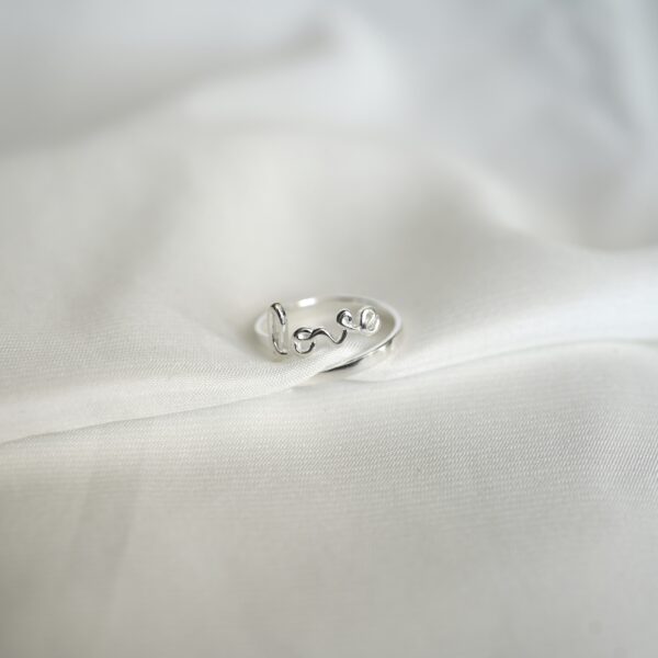 Schlichtes Love-Ring aus Silber auf weißem Stoff, christliche Schmuckmode, Geschenk für Gläubige.