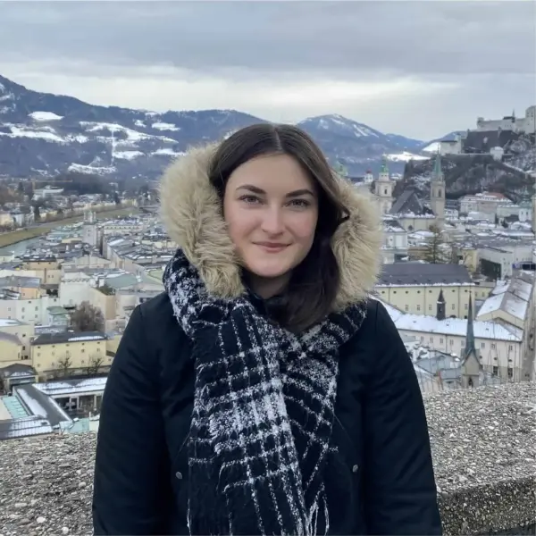 Mädchen mit Winterjacke und Fellkapuze vor historischem Stadtpanorama in Salzburg, Österreich.