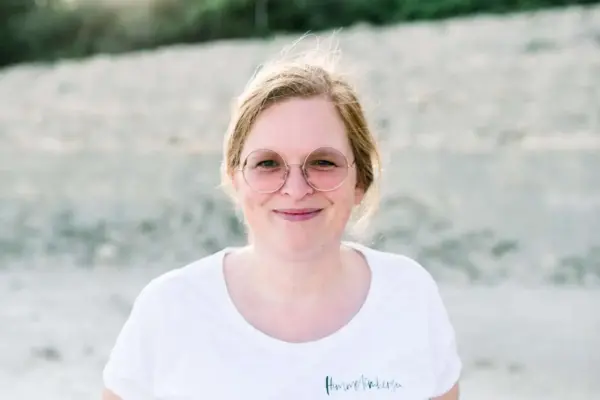 Fröhliche junge Frau mit Brille am Wasser, Sommer, Natur, Lifestyle.
