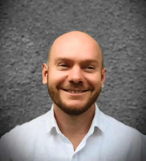 - Professioneller Mann mit freundlichem Lächeln vor grauer Wand.