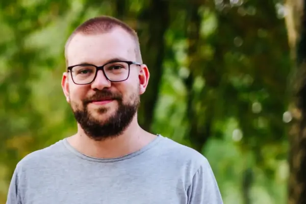 Junger Mann mit Brille und Bart im grünen Parkumfeld.