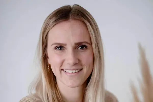 Fröhliche junge Frau mit blonden Haaren lächelt in weißem Raum.