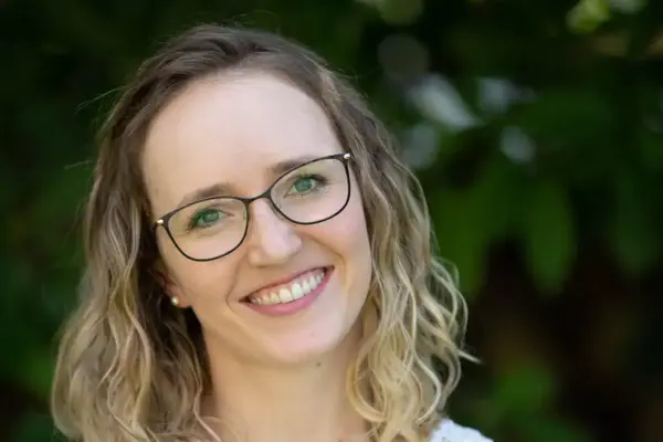 Freundliche junge Frau mit Brille, Naturhintergrund, Lächeln, hübsches Gesicht.